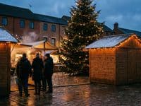 Drei Holzhütten mit Lichterketten auf einem Platz in der Dämmerung, Tannenbaum, nasses Kopfsteinpflaster